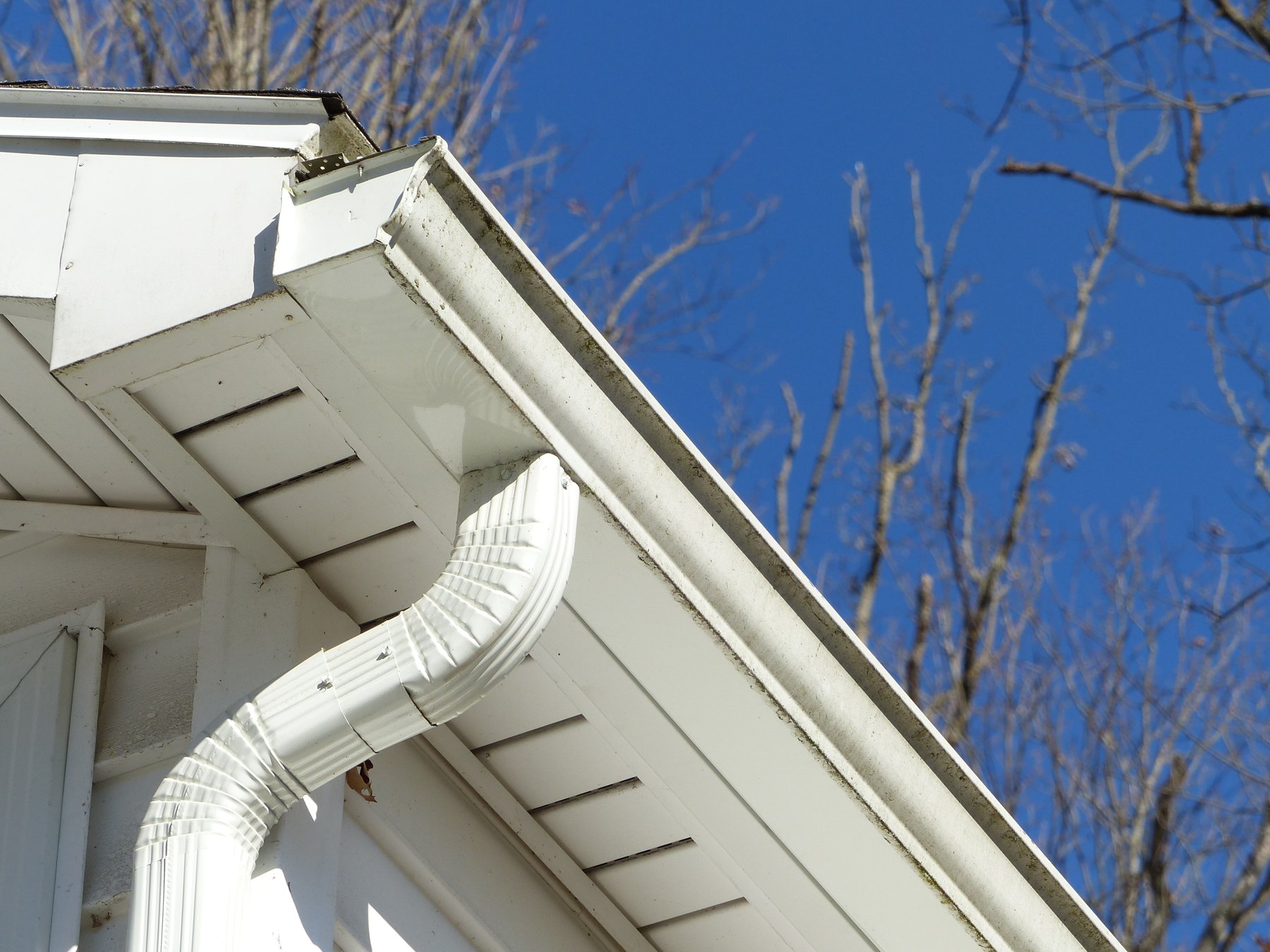 Close-up of a seamless gutter and corrugated downspout elbow on a home